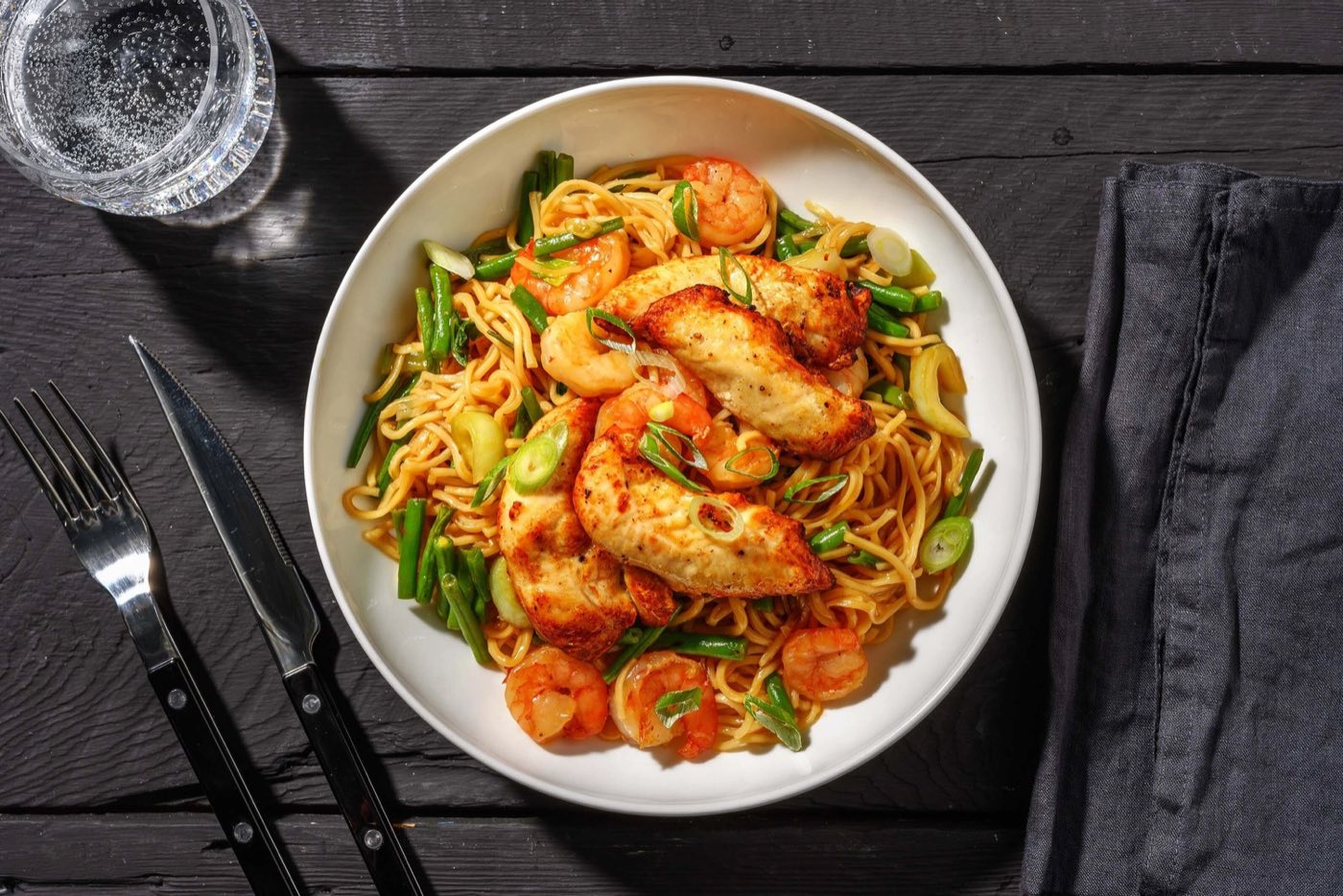 Overhead bowl of lo mein noodles with seared chicken, shrimp, scallions and green beans