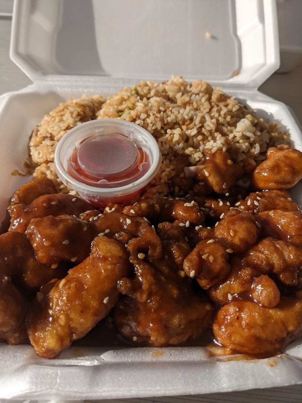 General Tso's chicken with sesame seeds and fried rice in a takeout box